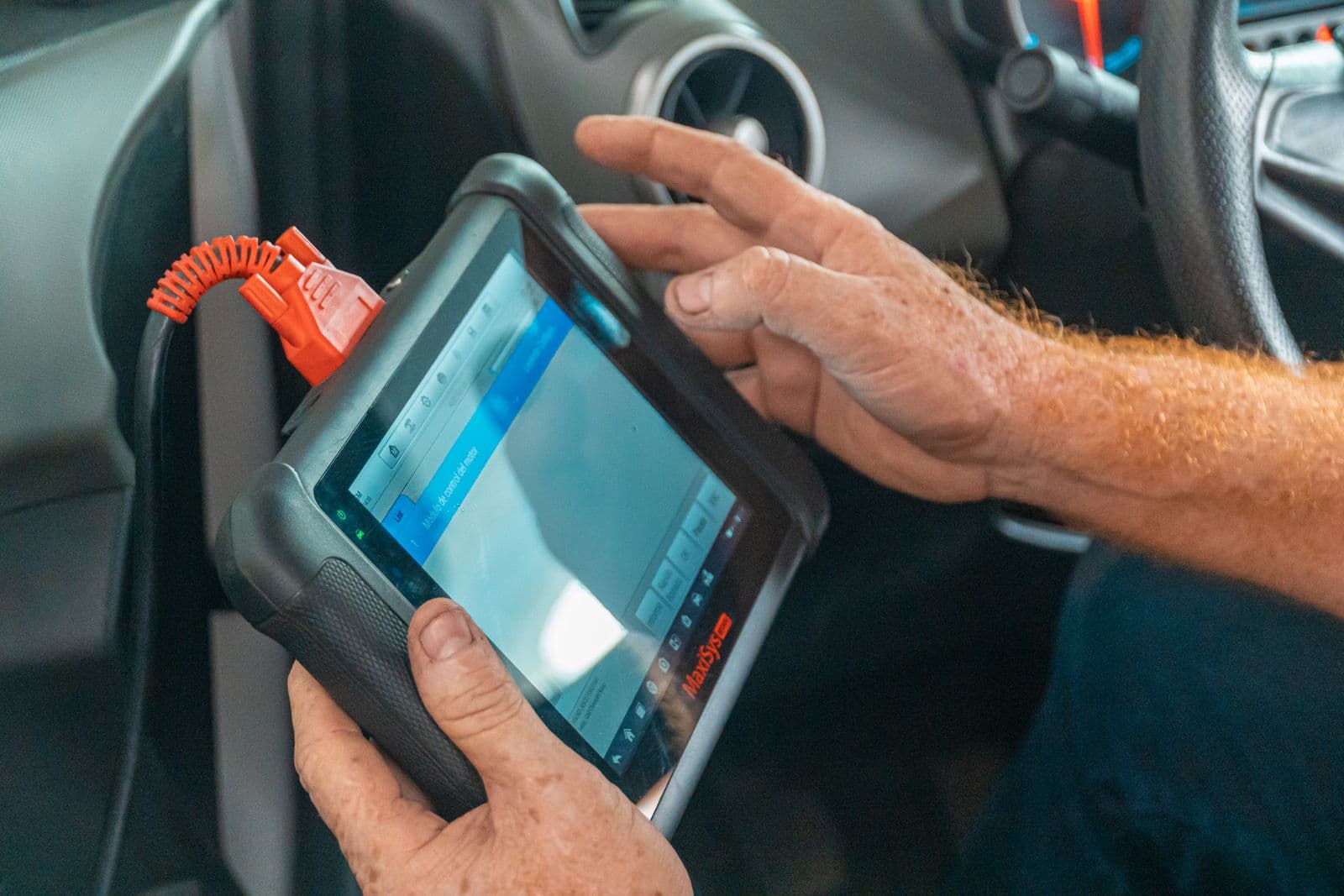 A technician's diagnostic tablet plugged into a car's OBD port